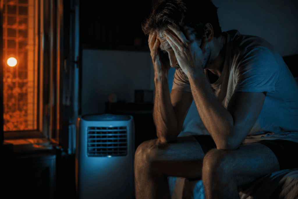 Une personne souffrant de la chaleur et du bruit d'un appareil avant de choisir un climatiseur mobile silencieux pour sa nuit.